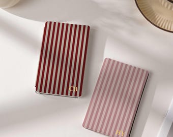 Puede incluir: Dos estuches rectangulares con rayas verticales. Uno presenta rayas de color rojo oscuro y blanco con las letras doradas CB, mientras que el otro presenta rayas de color rosa empolvado y blanco con las letras doradas HY. Acabado liso.