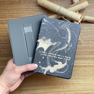 Puede incluir: Una funda para lector electrónico negra y dorada con un diseño de dragón y la cita "Un dragón sin su jinete es una tragedia. Un jinete sin su dragón está muerto."