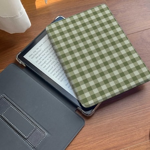 Puede incluir: Un lector electr&oacute;nico abierto con una funda a cuadros verdes y blancos. La pantalla muestra texto. El lector electr&oacute;nico est&aacute; en una funda gris con un soporte incorporado. La funda est&aacute; abierta, revelando la pantalla y el interior de la funda.