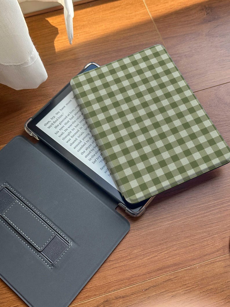 Puede incluir: Un lector electr&oacute;nico abierto con una funda a cuadros verdes y blancos. La pantalla muestra texto. El lector electr&oacute;nico est&aacute; en una funda gris con un soporte incorporado. La funda est&aacute; abierta, revelando la pantalla y el interior de la funda.