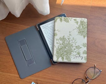 Może przedstawiać: Czarny czytnik e-booków w etui z kwiatowym wzorem. Etui ma napis "Lucky". Na zdjęciu widać również okulary i tubkę kremu do rąk.