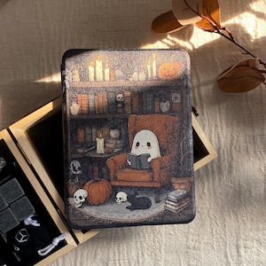 K&ouml;nnte beinhalten: Rechteckige Metallbox mit einer Halloween-Szene. Ein Geist liest in einem Sessel vor einem B&uuml;cherregal, umgeben von K&uuml;rbissen, Totenk&ouml;pfen und einer schwarzen Katze. Die Box ist mit Kerzen und B&uuml;chern dekoriert.