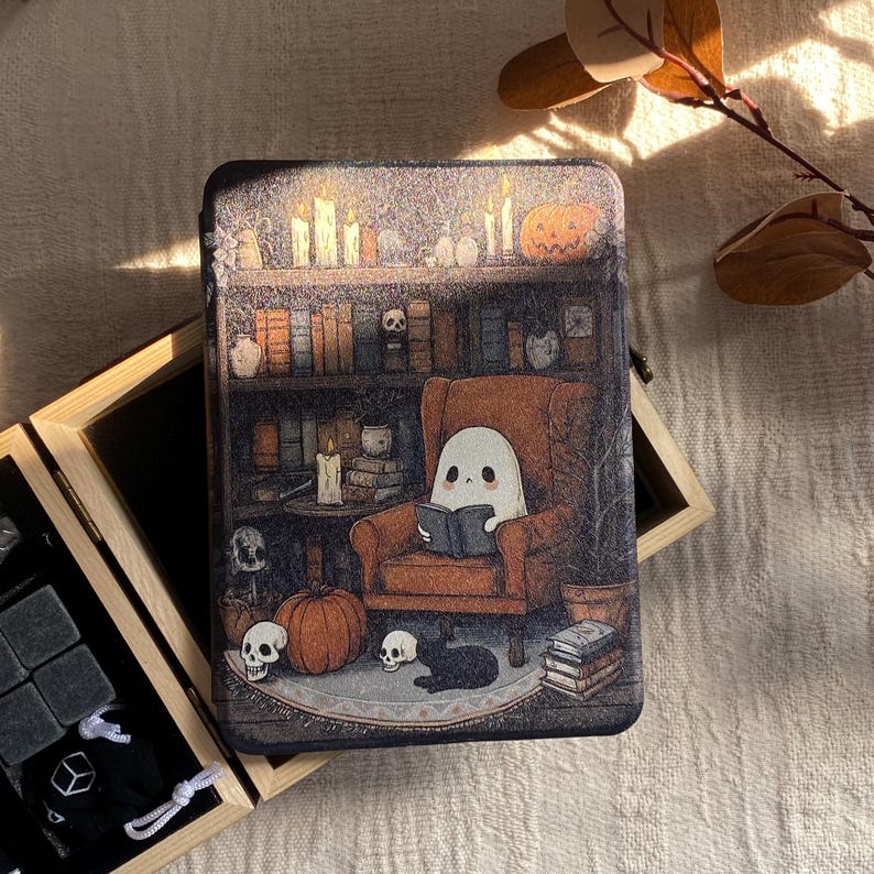 K&ouml;nnte beinhalten: Rechteckige Metallbox mit einer Halloween-Szene. Ein Geist liest in einem Sessel vor einem B&uuml;cherregal, umgeben von K&uuml;rbissen, Totenk&ouml;pfen und einer schwarzen Katze. Die Box ist mit Kerzen und B&uuml;chern dekoriert.