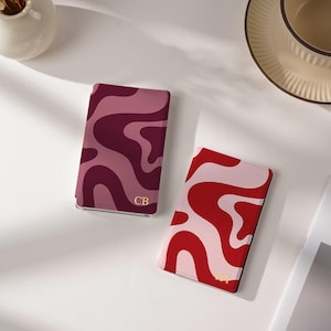 May include: Two rectangular card holders featuring wavy patterns. One holder displays shades of burgundy and mauve with the gold initials CB. The second holder features red and light pink wavy lines with the gold initials HY printed at the bottom.