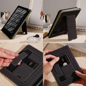 May include: Black e-reader case with a built-in stand. The case is dark gray with white stitching and a green interior. It features a card slot and a hand strap for secure handling. The e-reader displays a black and white pattern.