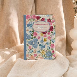 May include: A floral composition book with a cream background and a pattern of pink, blue, and purple flowers. The cover has a blue spine and the words "COMPOSITION BOOK" and "Lucky" are printed on the front.