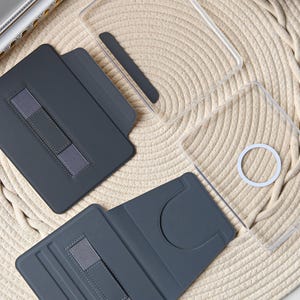 Puede incluir: Una colecci&oacute;n de fundas grises para tabletas con bandas el&aacute;sticas y cubiertas protectoras transparentes. Las fundas est&aacute;n abiertas y cerradas, mostrando su dise&ntilde;o. El fondo es una superficie tejida de tonos neutros.