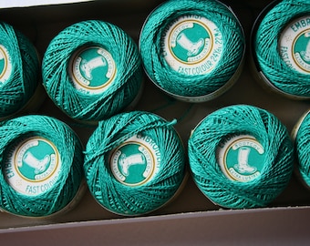 May include: A close-up of ten spools of teal green embroidery floss. Each spool has a white label with the text "BOOTCOV EMBROIDERY TWIST EXTRA LUSTRE FAST COLOUR 24Yds 22m" and a picture of a boot.