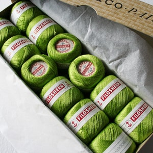 May include: A box filled with green yarn balls, each with a red label that reads "FILOSHEEN EMBROIDERY COTTON". The box is labeled "CO. PAISLEY"