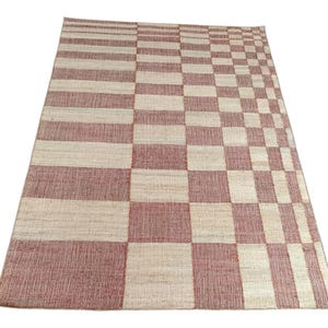 May include: A rectangular area rug featuring a woven pattern of alternating terracotta red and off-white squares. The design transitions from wide horizontal stripes on the left side to a smaller, dense checkerboard pattern toward the right edge.