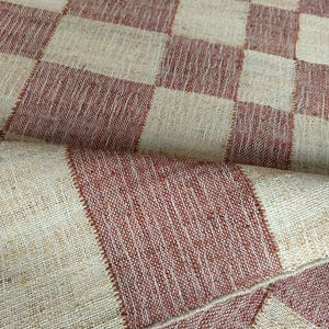May include: A woven textile fabric featuring a repeating checkerboard pattern in alternating squares of natural beige and terracotta red. The material has a visible coarse texture with distinct stitching lines defining each individual square.