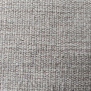 Pu&ograve; includere: Una vista ravvicinata di un tessuto intrecciato caratterizzato da una densa struttura a ricciolo. Il tessuto presenta una palette di colori neutri, che fonde fibre beige tenue e bianco sporco in un motivo a griglia costante e ripetitivo.