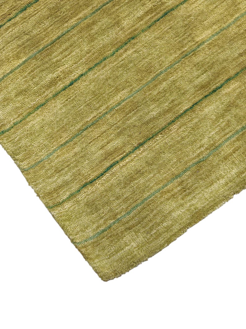 May include: A rectangular area rug featuring a textured, olive-green pile surface. The rug is decorated with a series of thin, parallel dark green stripes that run diagonally across the fabric, creating a simple linear pattern throughout the piece.