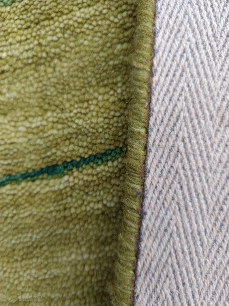 May include: A close-up view of a textured lime green rug with a dark green horizontal stripe. The rug features a thick, looped pile construction and a finished edge with a visible light gray herringbone pattern on the underside backing material.
