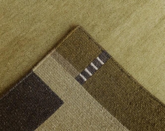 May include: A textured area rug featuring a geometric pattern in shades of olive green, sage, and dark brown. The corner displays a distinct block design with a small section of thin, parallel white lines set against a dark brown rectangular border.