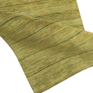 May include: A rectangular area rug featuring a textured olive green surface with thin, horizontal dark green stripes running across the length. The rug is partially folded over, revealing the soft, dense pile and the consistent linear pattern.