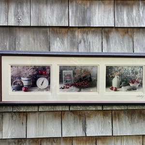 May include: Framed artwork featuring three panels with still life compositions. Each panel showcases arrangements of fruit, kitchen scales, and rustic containers. The color palette includes reds, whites, and browns, creating a vintage aesthetic. The artwork is displayed against a wooden background.