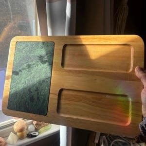May include: A rectangular wooden serving tray with a green marble insert and two recessed compartments. The tray is made of light-colored wood and has rounded corners. The marble insert has a natural, veined pattern.