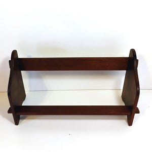 May include: A dark brown wooden bookshelf with a two-tiered design. The bookshelf has a rectangular base and a top shelf, connected by two side supports. The wood has a smooth finish and a natural grain.