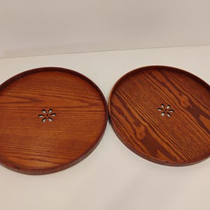 May include: Two round wooden trays with a rich brown finish. Each tray features a flower-shaped cutout in the center and a raised edge. The wood grain is prominently displayed, adding to the natural aesthetic. These trays are ideal for serving or display.