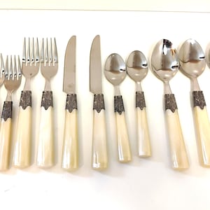 May include: A set of vintage silverware with stainless steel blades and tines. The handles are a creamy off-white color with a decorative silver-toned band. The set includes forks, knives, and spoons, perfect for a formal dining setting.