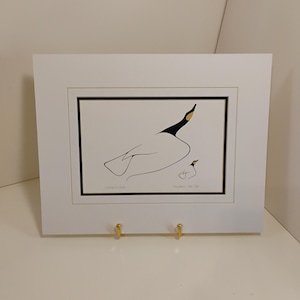 Puede incluir: Una impresión artística enmarcada con un dibujo lineal minimalista de un ganso y un gansito. La obra de arte es principalmente en blanco y negro, con un toque de dorado en el pico del ganso. La impresión está enmarcada en blanco.