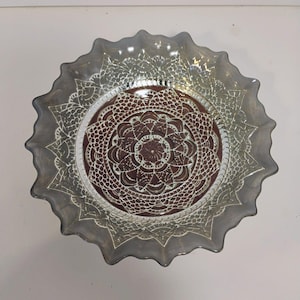 May include: A decorative glass plate with a scalloped edge. The plate features a central maroon design with a white lace-like pattern. The outer rim is a smoky gray color, adding a vintage aesthetic.