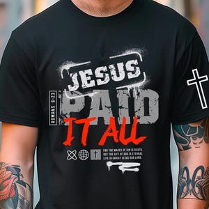 Puede incluir: Camiseta negra con el texto "JESUS PAID IT ALL" en blanco y rojo. Una cruz blanca está en la manga. La camiseta también tiene el texto "Romanos 6:23" y otro texto religioso. La imagen también incluye las palabras "ONLY DIGITAL DOWNLOAD" e "INSTANT DOWNLOAD".