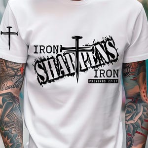 Puede incluir: Camiseta blanca con un diseño gráfico negro que presenta una cruz hecha de clavos y el texto "Iron Sharpens Iron Proverbs 27:17".