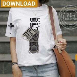 May include: White t-shirt with the word "BLESSED" in a distressed, gray and black design. A black cross is on the left sleeve. The words "SIMPLY" are above the word "BLESSED".