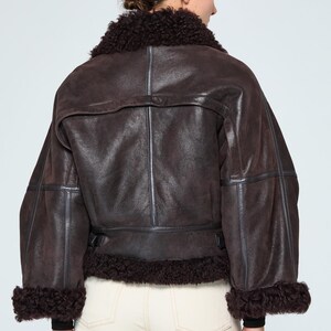 Back view of a handcrafted women's leather aviator coat showing tailored handstitched seams and high-end outerwear construction.

Elegant woman outdoors in winter wearing a warm genuine leather shearling bomber coat with vintage aviation style.