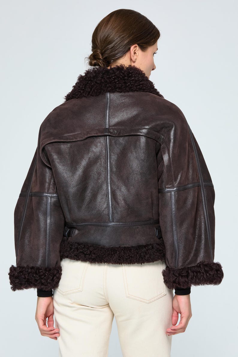 Back view of a handcrafted women's leather aviator coat showing tailored handstitched seams and high-end outerwear construction.

Elegant woman outdoors in winter wearing a warm genuine leather shearling bomber coat with vintage aviation style.