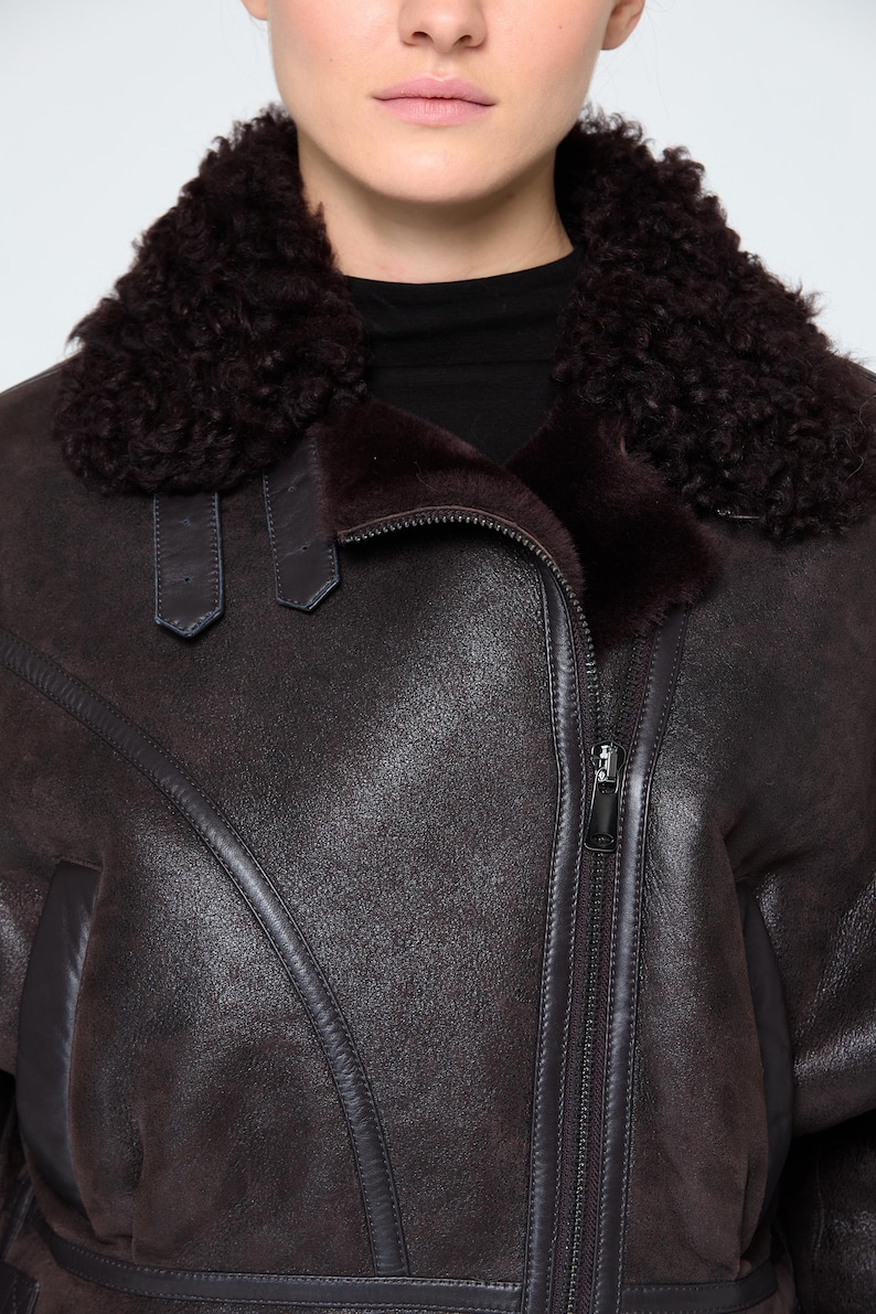 Detail shot of heavy-duty metal buckles, leather straps, and soft sheepskin wool on a bespoke B3 winter jacket for women.