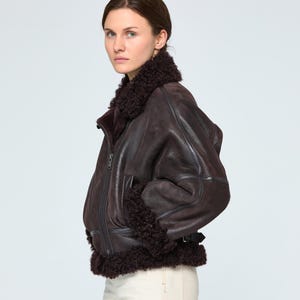 Close-up texture of genuine brown sheepskin leather and premium natural shearling fur lining on a luxury winter bomber jacket.