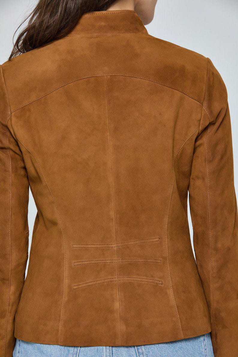 May include: A brown suede jacket with a tailored fit. The jacket features a stand-up collar, long sleeves, and a series of horizontal stitched details near the waist. The back view showcases the jacket's design and construction.