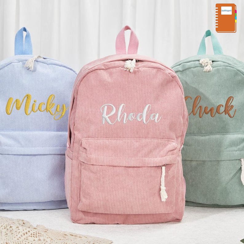 May include: Three corduroy backpacks in pastel colors: light blue, pink, and green. Each backpack has a front pocket and a top handle. The names "Mickey", "Rhoda", and "Chuck" are embroidered on the front in contrasting colors.