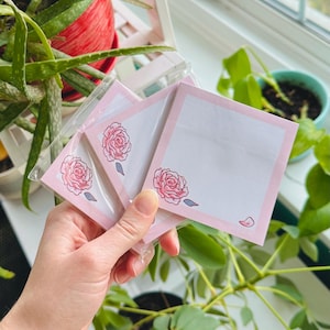 May include: Three pink sticky note pads with a floral design. Each pad has a pink rose with a light pink outline. The pads are packaged in clear plastic.