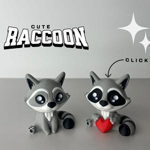 Könnte beinhalten: Zwei graue Waschbär-Figuren mit schwarzen Augen und Nasen. Ein Waschbär hält ein rotes Herz. Der Text "Cute Raccoon" befindet sich über den Figuren und der Text "Clicker" befindet sich über dem Waschbär, der das Herz hält.