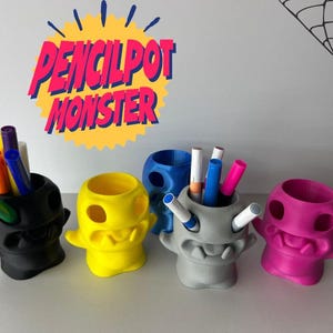 Könnte beinhalten: Eine Sammlung farbenfroher, monsterförmiger Stifthalter. Die Stifthalter sind schwarz, gelb, blau, grau und pink und halten Stifte und Marker. Der Text "PENCILPOT MONSTER" ist über den Stifthaltern zu sehen.