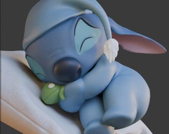 Może przedstawiać: Pluszowa zabawka Stitch z Lilo & Stitch, w kolorze niebieskim i białym, w niebiesko-białej czapce do spania, trzymająca zielony liść i śpiąca na białej poduszce.