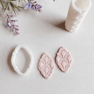 May include: Two pink polymer clay earrings with a geometric pattern, a white silicone mould for making earrings, and a white rolling pin with a textured design.