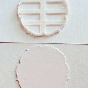 Peut inclure: Un moule en plastique blanc avec un bord festonné et une grille à l'intérieur. Le moule est sur une surface blanche.