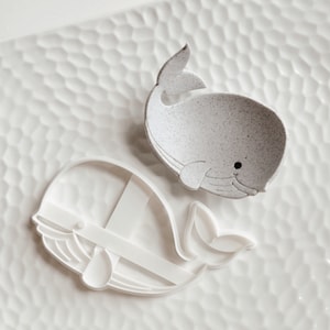 Peut inclure: Deux emportes-pièces en forme de baleine blanche, l'un avec une finition mouchetée, sur une surface texturée blanche.
