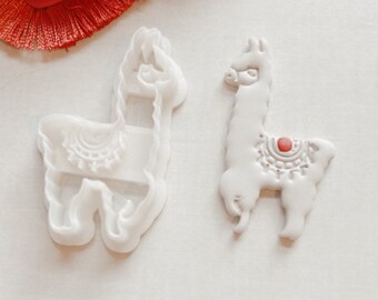 May include: Two white plastic llama cookie cutters. One cutter has a detailed design on the llama's back. The other cutter is a simple outline of a llama.