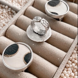 May include: Four silver rings with black and white patterned inlays. The rings are displayed in a ring holder with beige fabric lining.