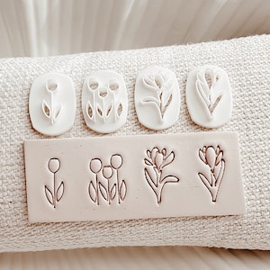May include: Set of six white polymer clay stamps featuring floral designs. The stamps are arranged in two rows of three. The top row features three different floral designs, while the bottom row features the same three designs in a smaller size. The stamps are on a white background.