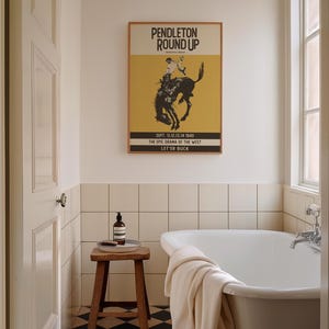 May include: A bathroom scene featuring a framed "Pendleton Round Up" poster with a rodeo theme. The poster is above a white bathtub. A small wooden stool holds a bottle and brush. The room has white tile and a black and white checkered floor.