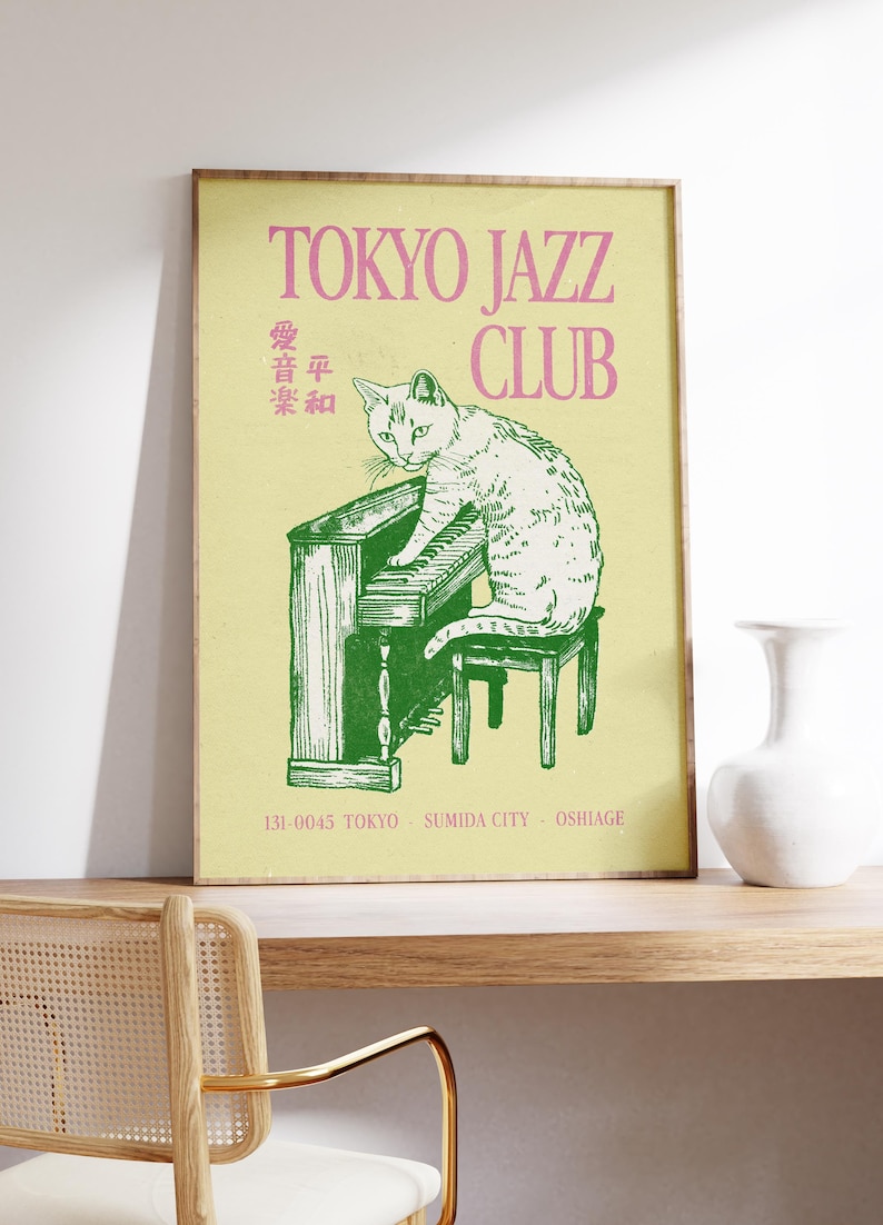 May include: A framed poster with a light yellow background features a green illustration of a cat playing a piano. The text "TOKYO JAZZ CLUB" is in pink. Japanese text and address details are also present.