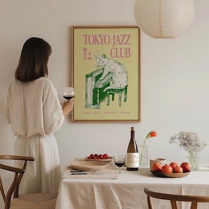 May include: A framed poster with a cat playing a green piano, with the text "TOKYO JAZZ CLUB" in pink. The poster is in a room with a table set for a meal, including a bottle of wine and a glass of red wine.
