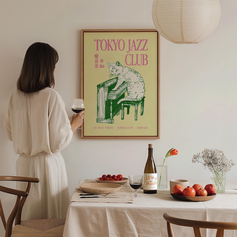 May include: A framed poster with a cat playing a green piano, with the text "TOKYO JAZZ CLUB" in pink. The poster is in a room with a table set for a meal, including a bottle of wine and a glass of red wine.